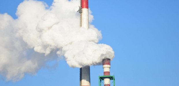 Photo of two factory chimneys with steam coming out of them against a blue sky.